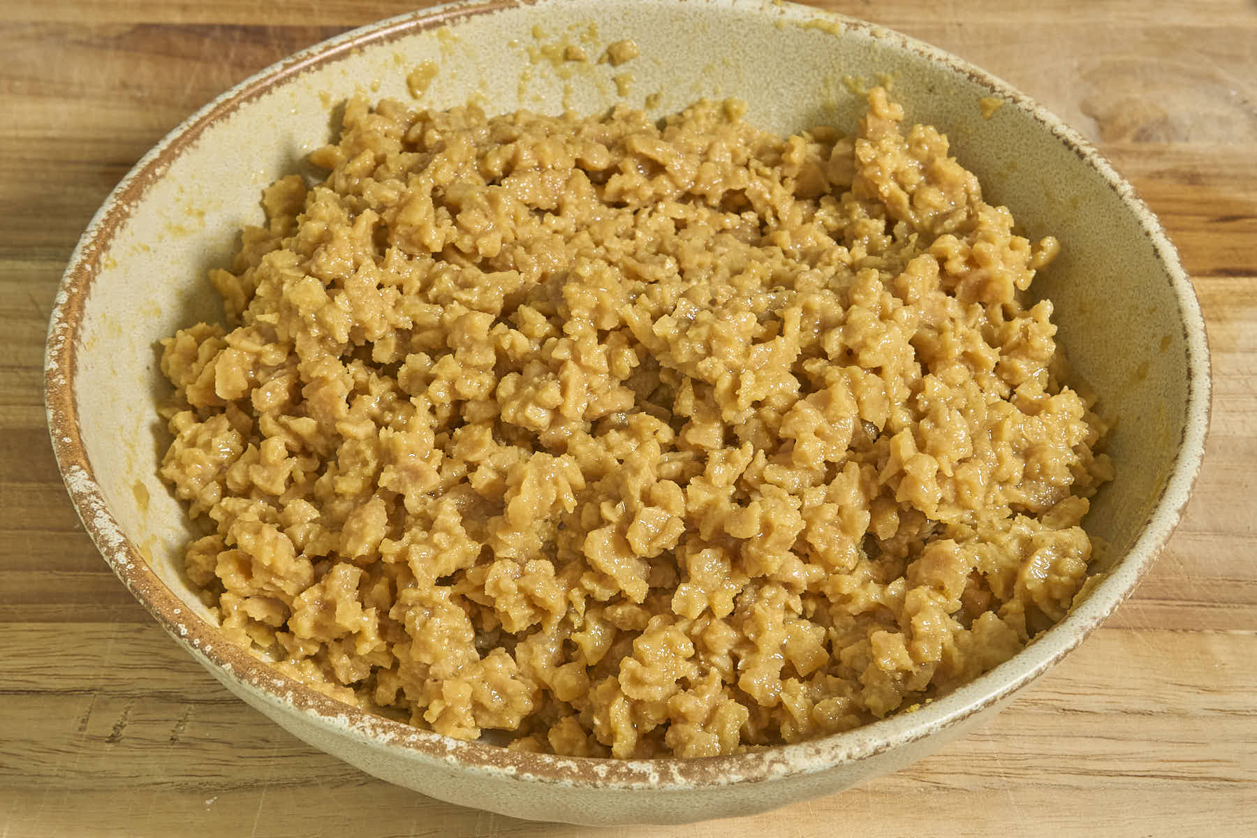 A bowl of marinated TVP and beaten egg, mixed, on a wooden surface.