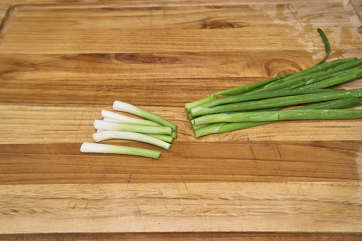 Sliced green onions on a wooden cutting board.