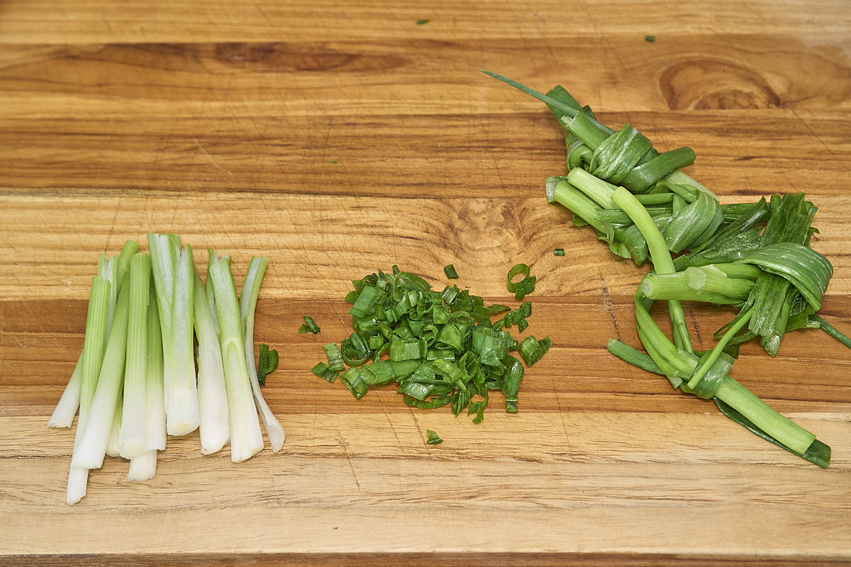 Green onions that are sliced, chopped, and made into knots on a wooden cutting board.