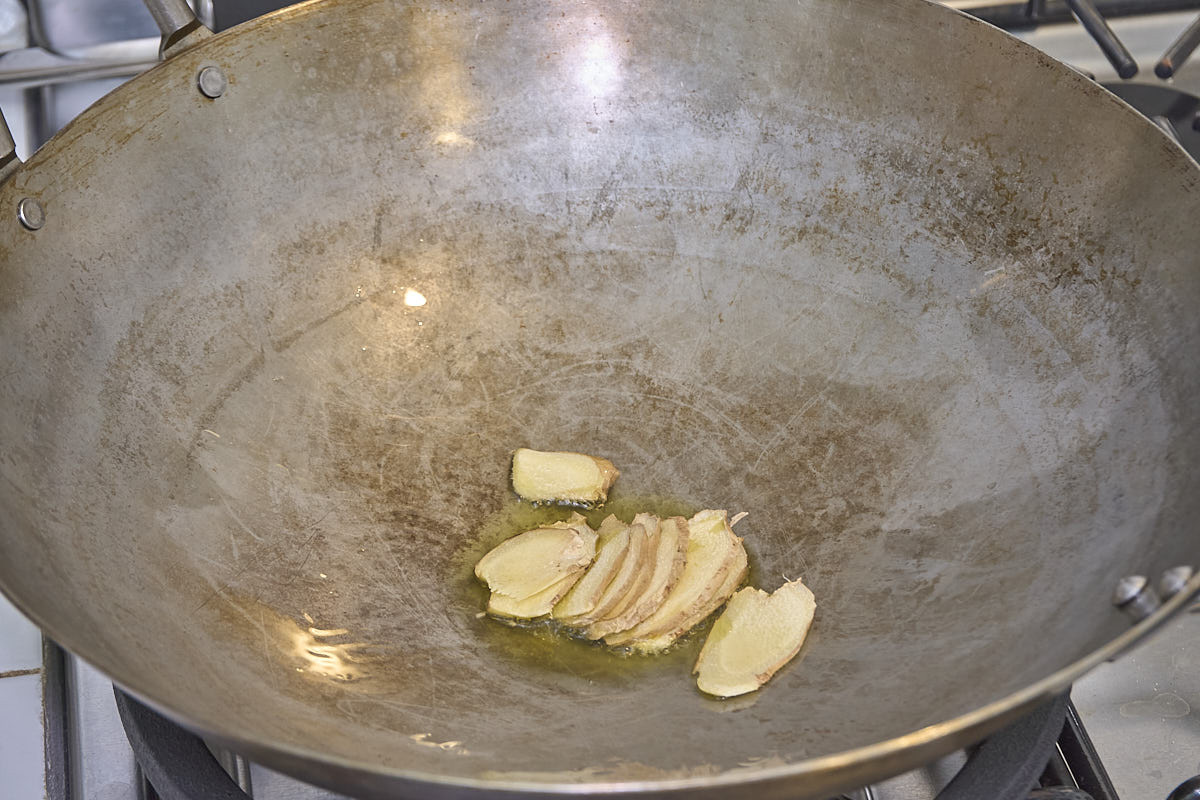 Thin slices of ginger cooking in oil in a wok on stove.